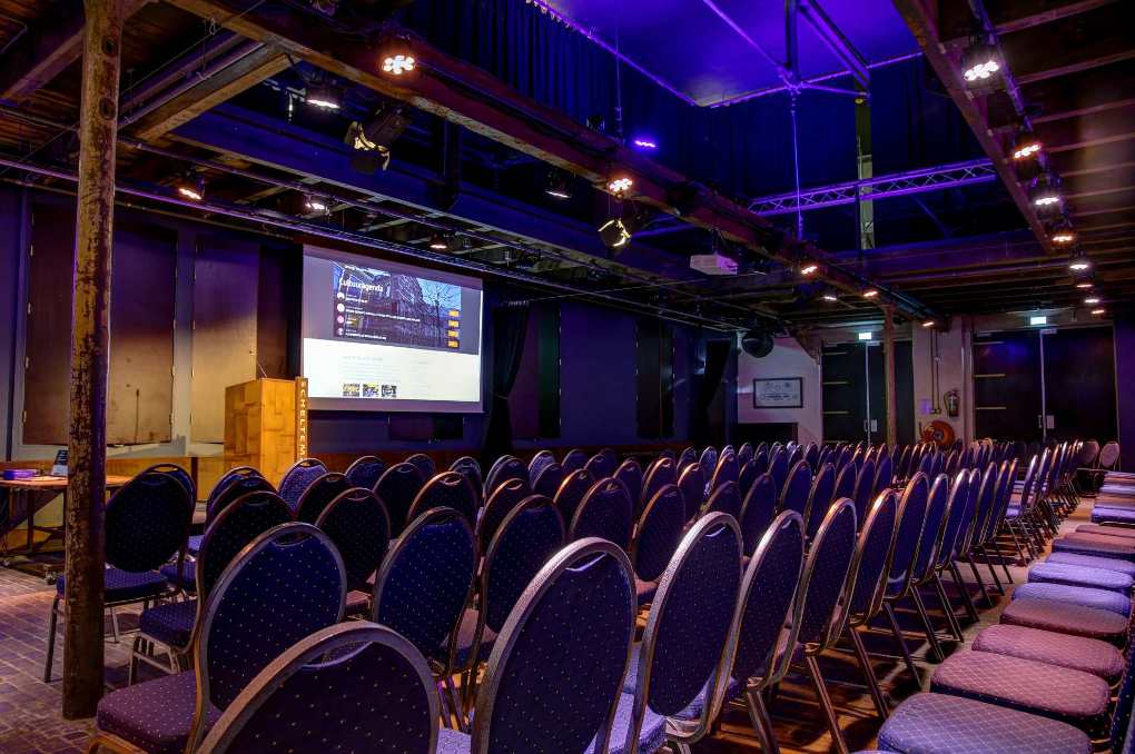 De Theaterzaal met een groot projectiescher, en heel veel stoelen in Scheltema Leiden