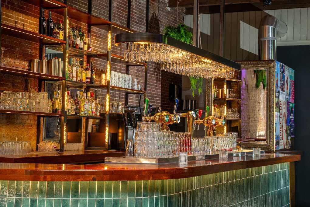 A bar in a restaurant with a green tiled wall.