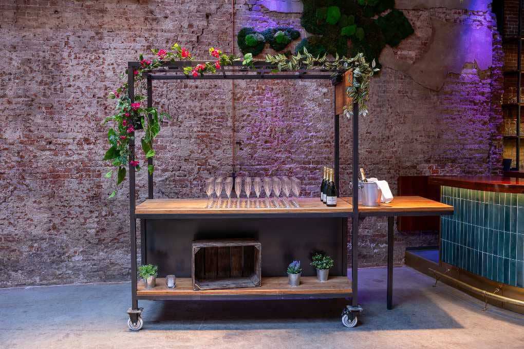 A bar cart in a brick building with plants on it.